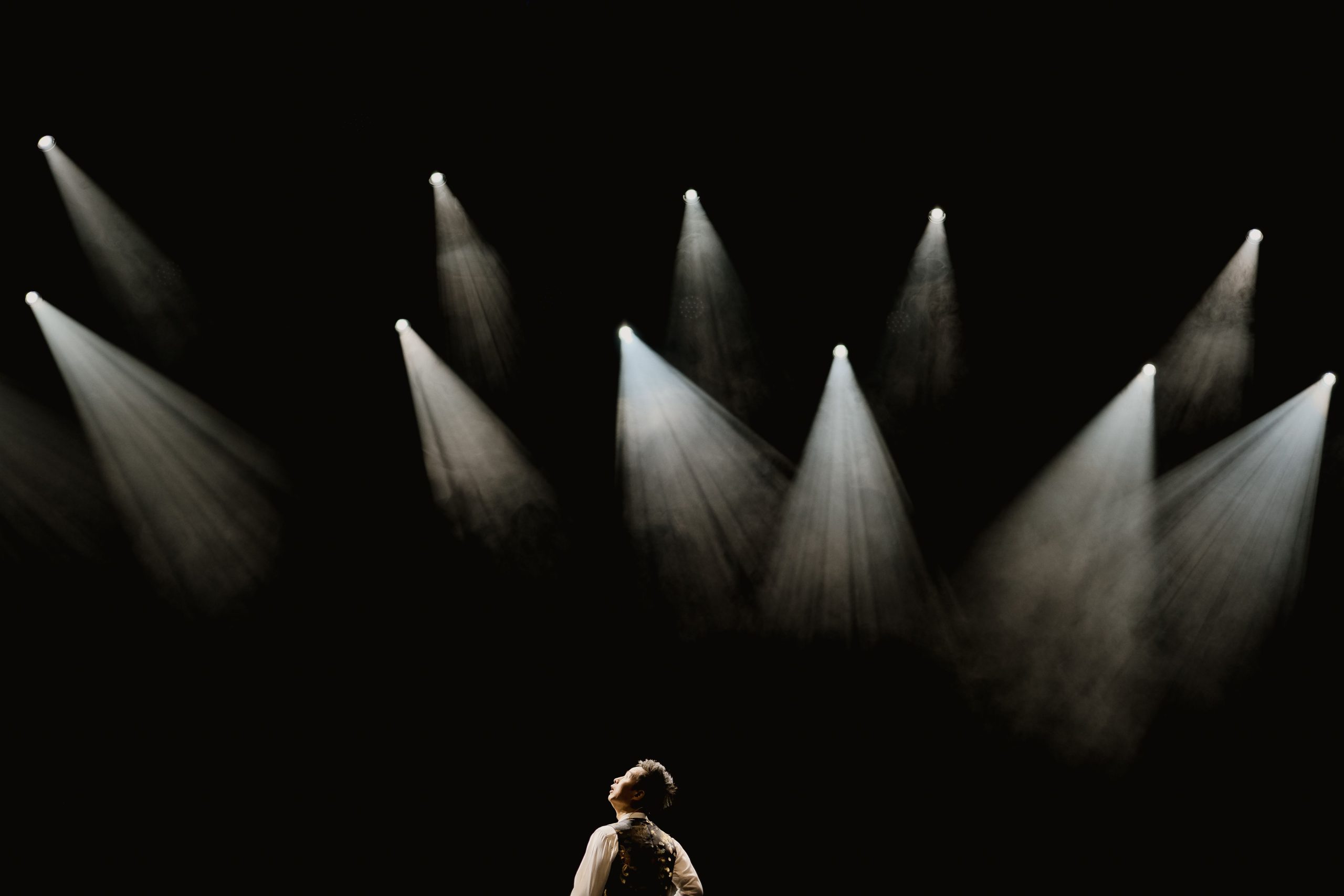 A solo performer stands confidently in a warm spotlight on a dark stage, symbolizing being the center of attention