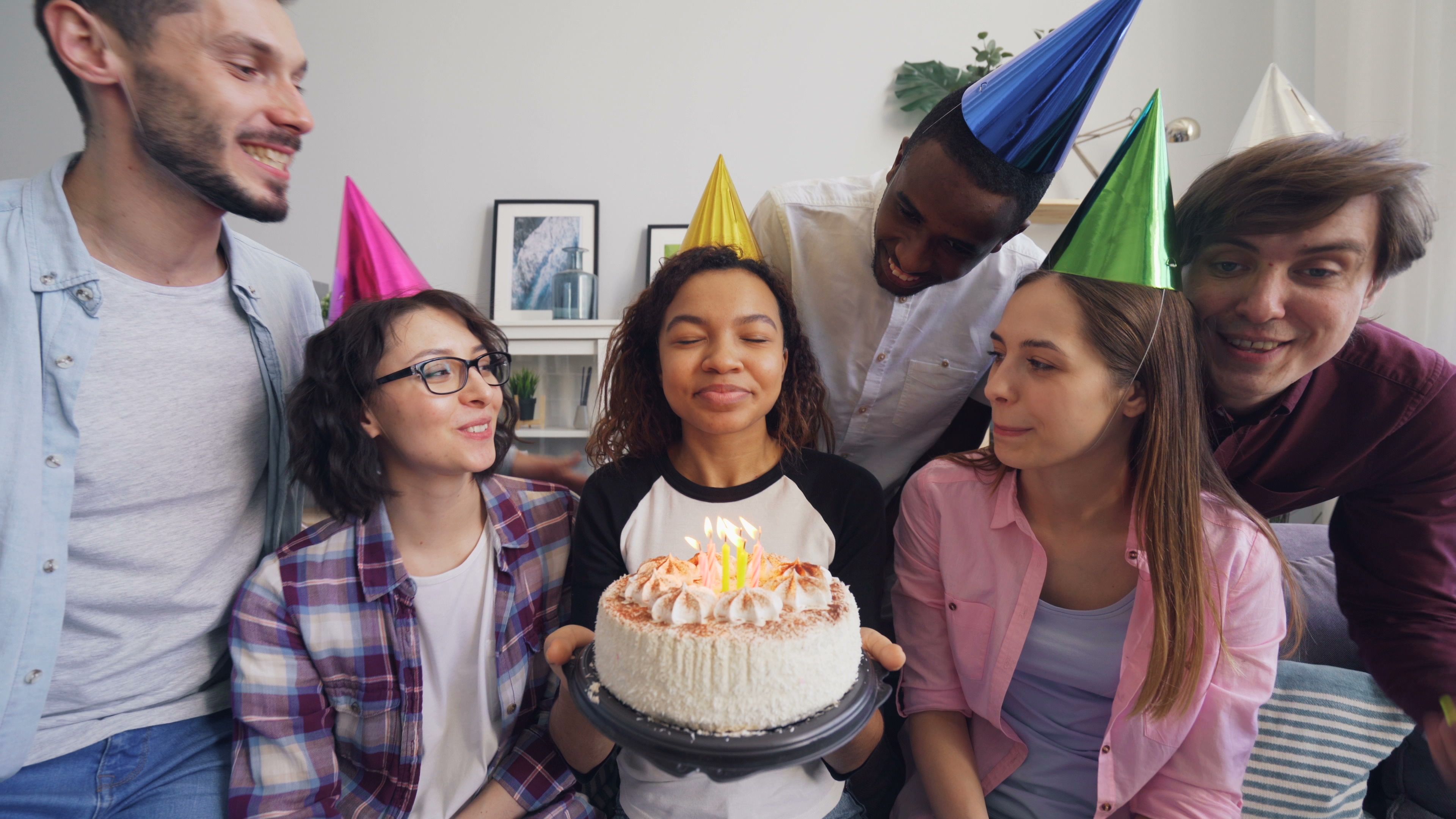 A group of friends celebrating a birthday together with a cake and party hats indoors