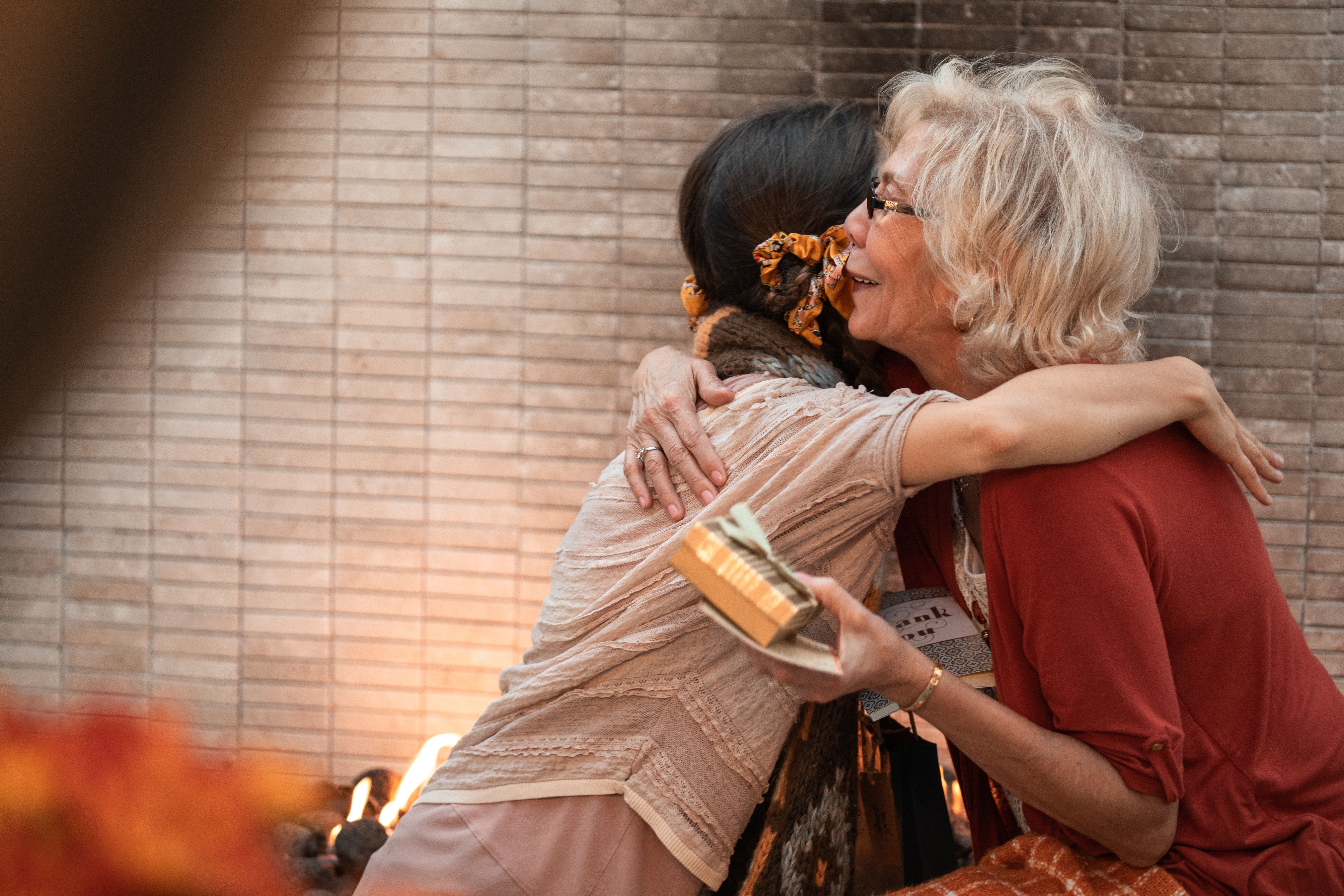 An elderly woman and a younger woman sharing a heartfelt hug while holding a gift