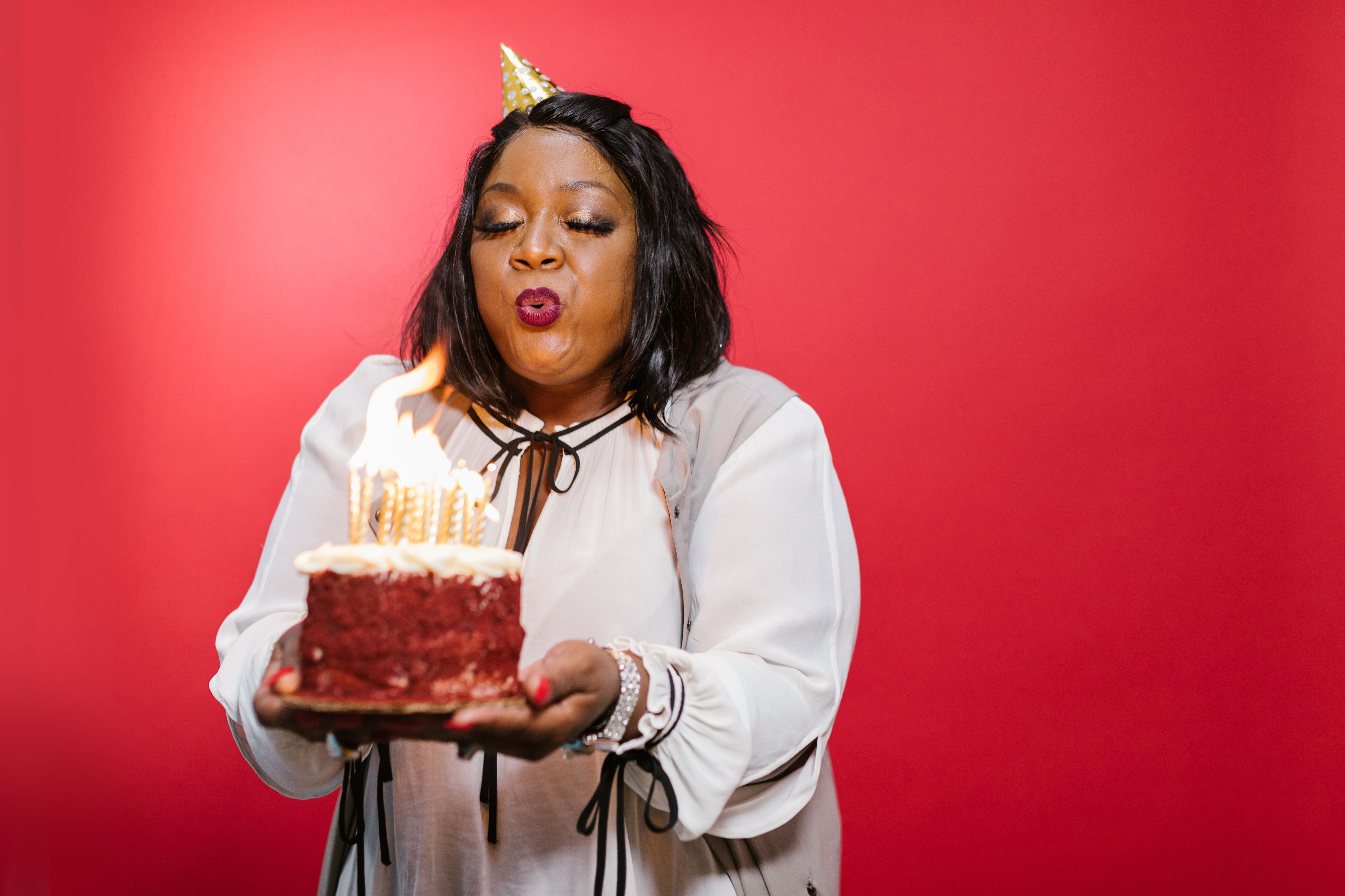 A joyful woman blowing out birthday candles on a red velvet cake