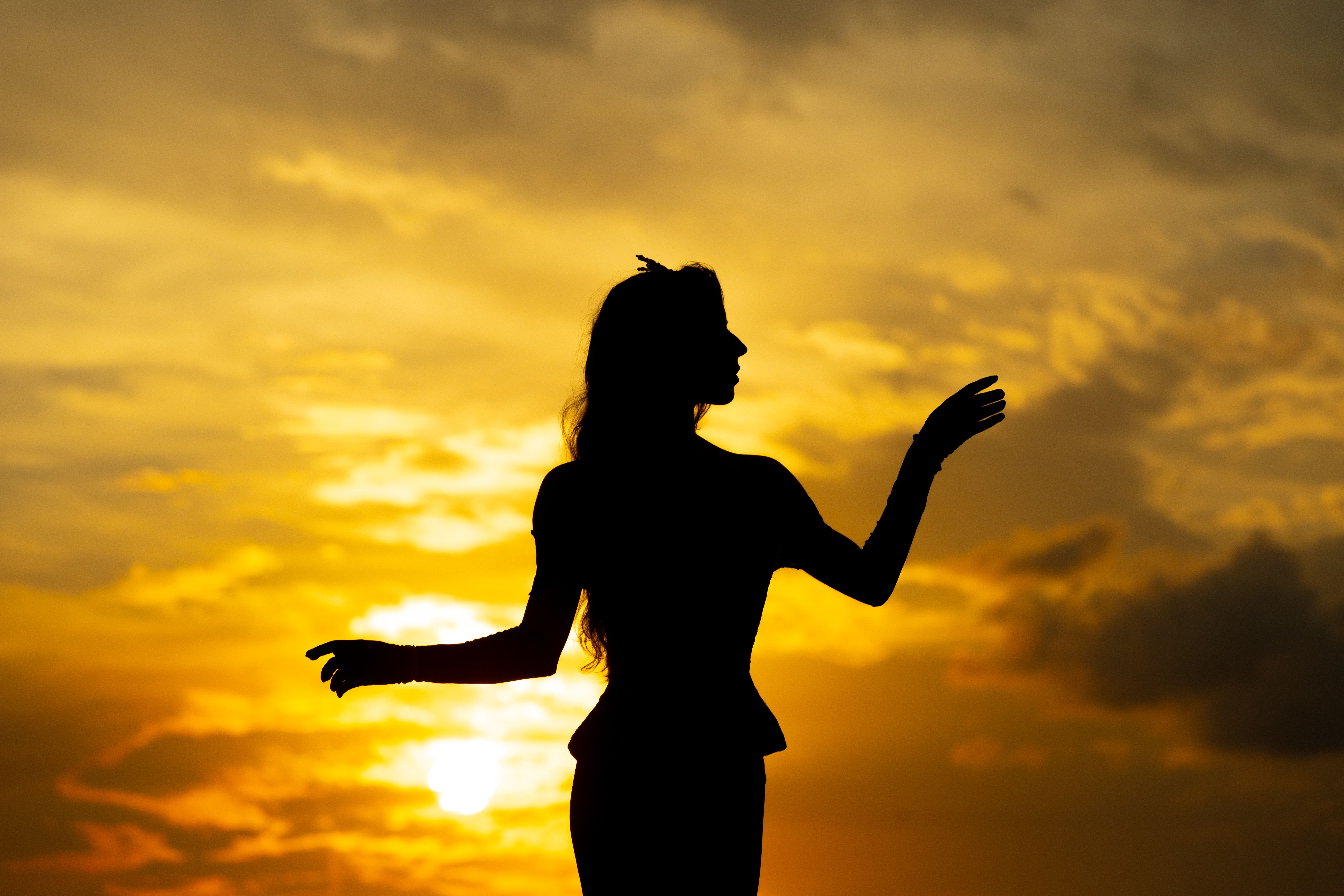 Silhouette of a woman dancing joyfully against a vibrant sunset sky